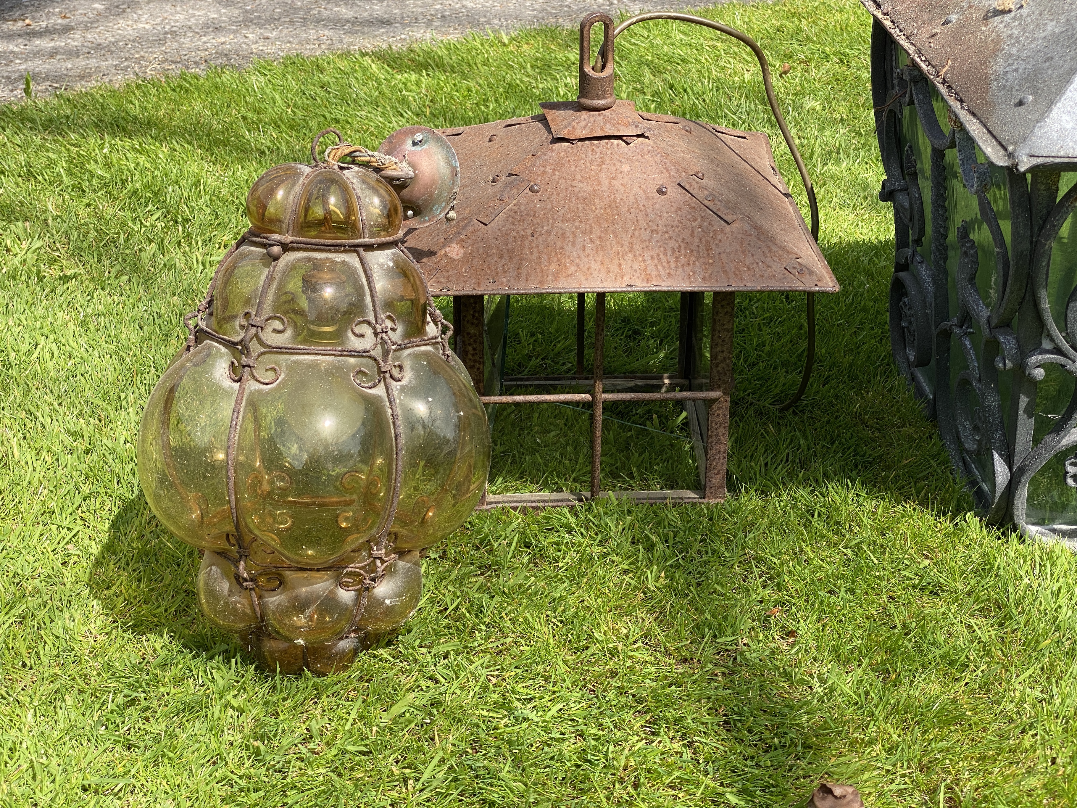 A wrought iron square shaped hanging lantern, height 67cm x 50cm, width; another, smaller lantern and a 1950’s Murano blown amber glass and wire work lantern (3)